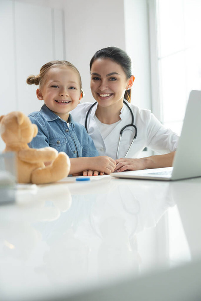 Friendly pediatrician and happy little kid posing for camera indoors - Photo, image