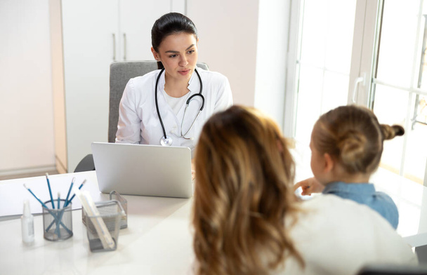 Serious female doctor talking to small girl in clinic - Foto, Imagem