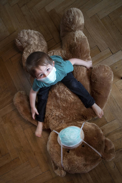 Coronavirus, Covid-19, Çocuk ve koruyucu maskeli oyuncak ayısı evde karantina altında.  - Fotoğraf, Görsel