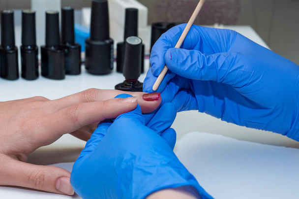 Manicure specialist applying red nail polish on healthy natural female nails in beauty salon - Fotografie, Obrázek