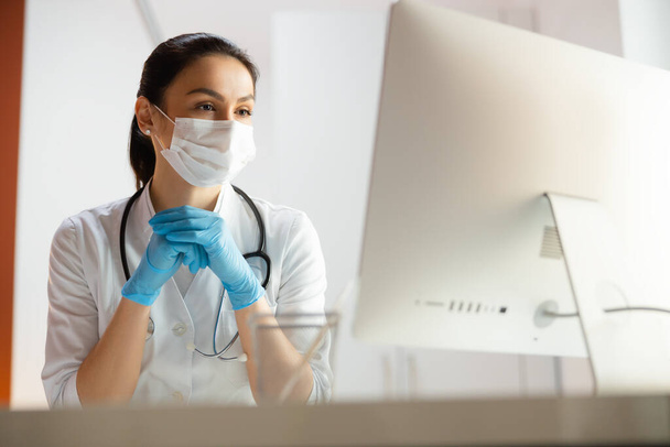 Beautiful doctor in medical mask doing tasks at laptop - Photo, image