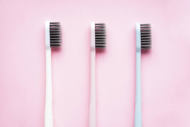 Vlakke lay compositie van veelkleurige tandenborstels op een roze achtergrond. Close-up - Foto, afbeelding