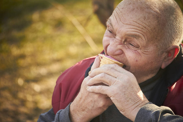 Вісімдесятирічний чоловік гуляє в громадському парку, їсть морозиво у вафельній чашці
 - Фото, зображення