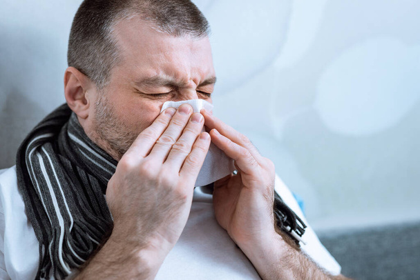 Hombre soplando la nariz en el tejido teniendo fiebre acostado en la cama
 - Foto, imagen