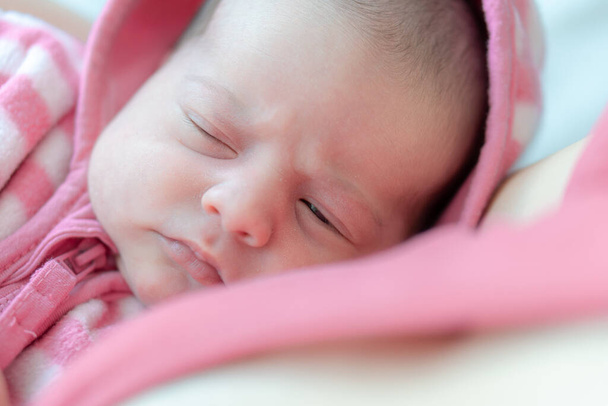 Newborn in the arms of mom. Portrait of a newborn baby. Close-up face of newborn baby with open eyes. Baby is looking into the lens close up. Newborn baby in a pink blouse. - Foto, immagini