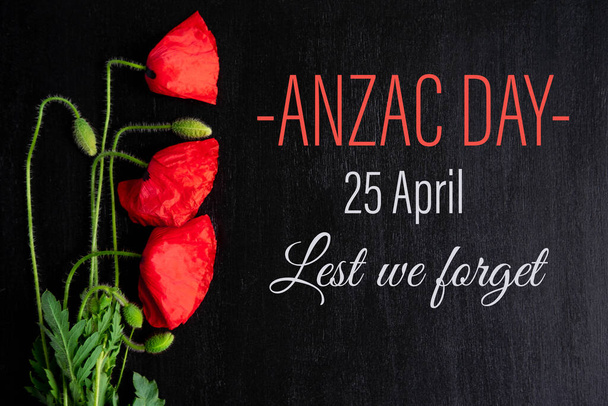 Anzac day. Greeting card with the inscription and poppy flowers on a black background. - Foto, Imagen