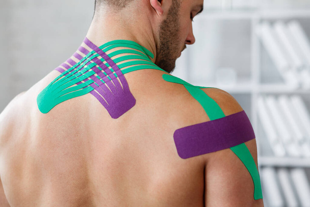 Kinesiology taping. Kinesiology tape on patient neck. Injured trapezius muscles treatment of young male athlete. Post traumatic rehabilitation, sport physical therapy, recovery concept - Fotografie, Obrázek