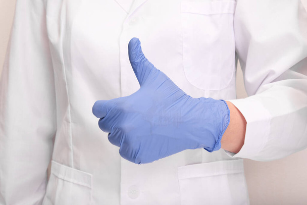A doctor in uniform and blue nitrile gloves showing thumb up. - Fotó, kép