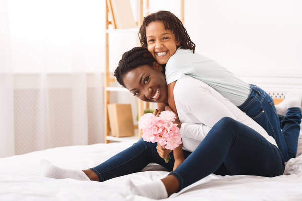 czarny dziewczyna gratulacje jej mama z kwiaty w domu - Zdjęcie, obraz