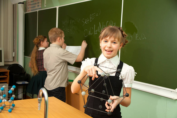 Школьница возле доски держит в руках модель молекул
 - Фото, изображение