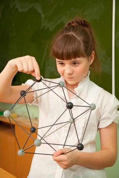 Das Schulmädchen neben der Tafel hält das Modell der Moleküle in den Händen - Foto, Bild