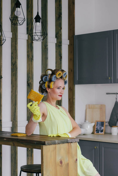 Girl blonde in curlers and a yellow dress rubs a glass - Фото, изображение