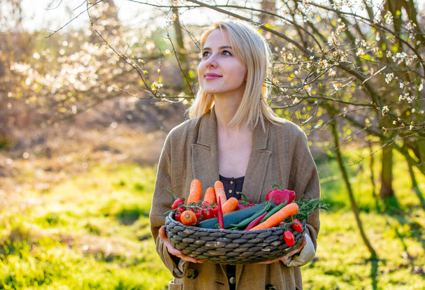 Blonde Frau mit Gemüse im Korb im blühenden Garten im Frühling  - Foto, Bild