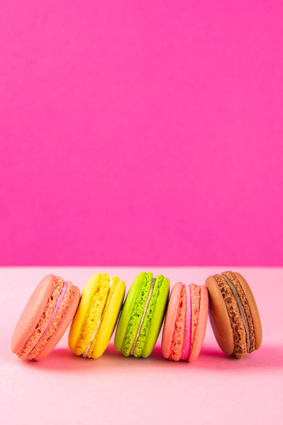 Colorful macaroons stand in a row against a pink background. Close-up with clear space - Φωτογραφία, εικόνα