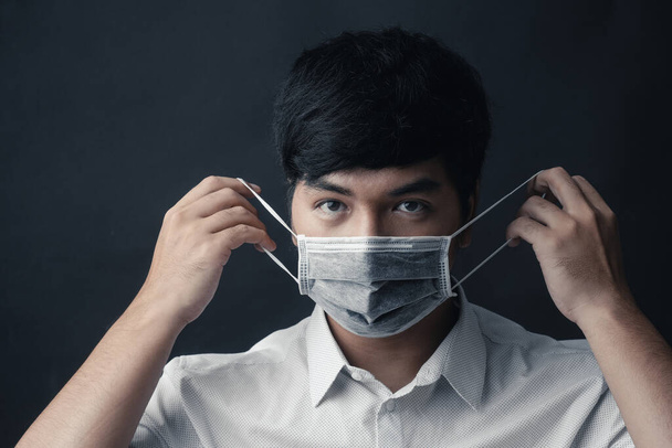 Aziatische man met medisch masker op zijn gezicht in zwarte achtergrond - Studio portret - Foto, afbeelding