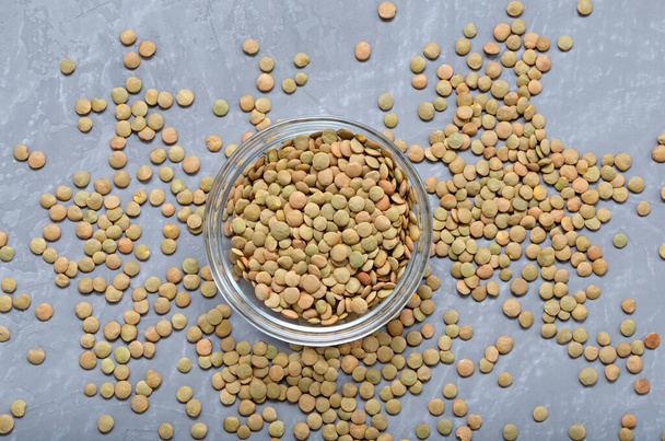 lentils in a glass bowl and scattered nearby on a gray background with copy space. healthy food template. veganism. lean food. - Fotó, kép
