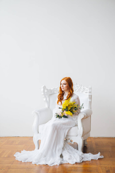 Portrait of a red-haired beautiful girl with a Mimosa in a long white dress. Spring concert. Toning. - Foto, afbeelding