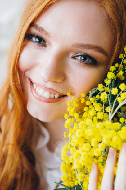 Portrait of a red-haired beautiful girl with a Mimosa in a long white dress. Spring concert. Toning. - Foto, Imagen