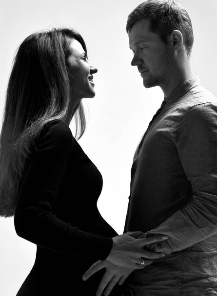 Pregnant girl in black dress and her husband. He hugging her belly, they going to kiss, posing isolated on white. Close up - Photo, image