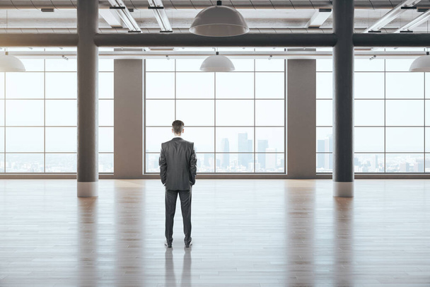 Businessman standing in gallery interior with empty wall and columns and looking to window.  Workplace and lifestyle concept. - Foto, Imagem