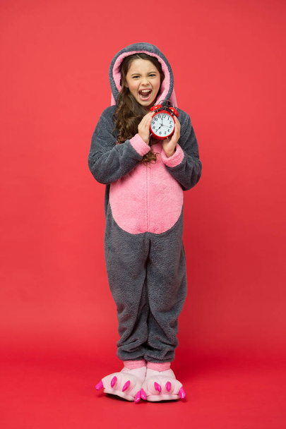 Early rise. angry kid in kigurumi pajama hold alarm clock. time to wake up. sweet dreams. good morning to you. people and bedtime concept. little girl wear easter bunny costume. Counting time - Foto, immagini