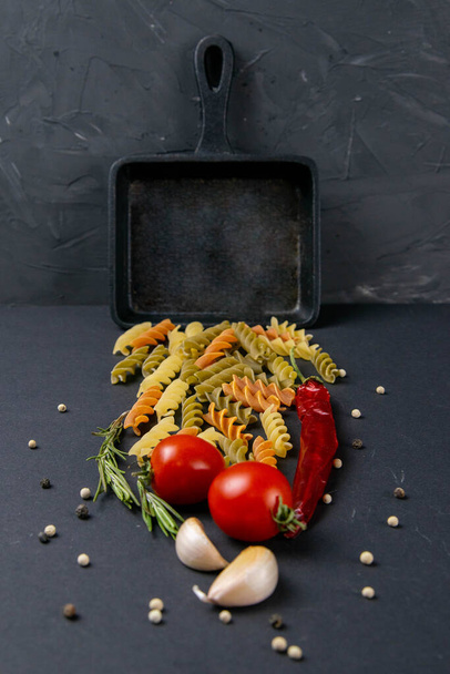 Итальянская еда сырые макароны с помидорами, розмарином, острым перцем и чесноком в небольшой сковороде. Вид спереди, крупным планом
 - Фото, изображение