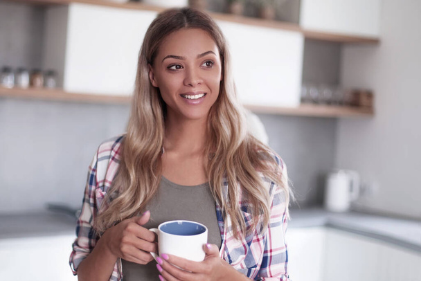 cute young woman with mug standing in kitchen - Zdjęcie, obraz