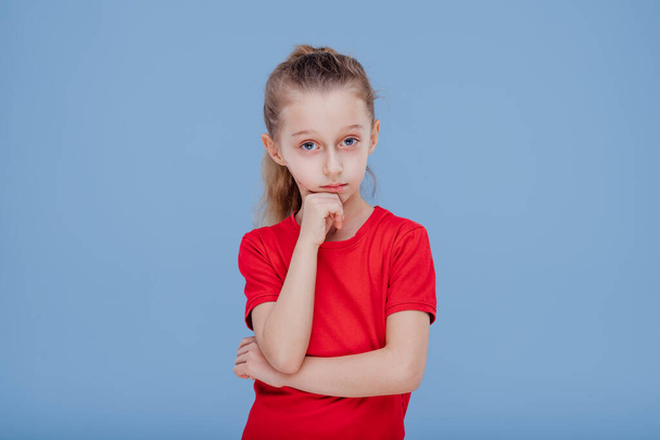 Thoughtful doubtful little girl in red t shirt touching chin - Photo, image