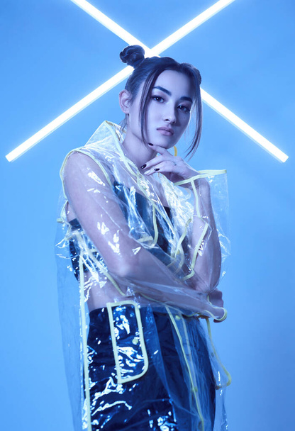 Портрет елегантної азіатської жінки в модному плащі навколо яскравих неонових світильників, що виставляються в студії - Фото, зображення
