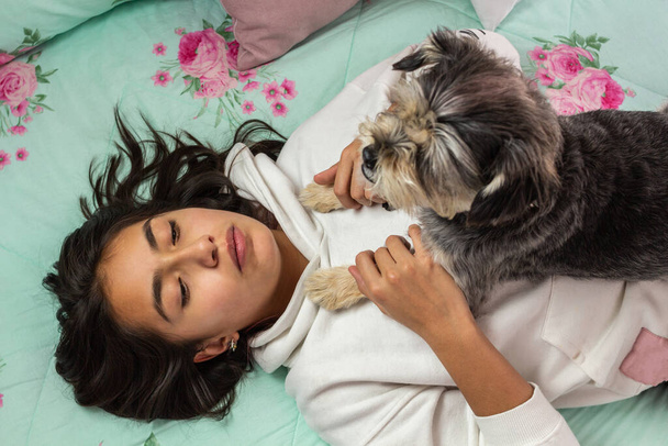 Adolescente em seu quarto mimando seu cão em sua cama, tomando suas patas
 - Foto, Imagem