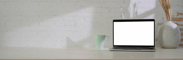 Close up view of minimal workspace with blank screen laptop, kubek, dekoracja i przestrzeń na białym stole z cegły tle ściany   - Zdjęcie, obraz