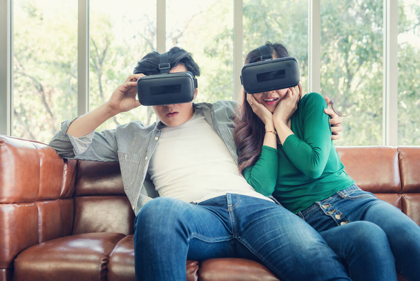 Young Couple Having Fun While Watching Video Via Virtual Reality Together. Couple Love Having Enjoyment With Electronic VR Goggles Gaming on Couch. Entertainment Innovation/Lifestyles Concept - Photo, Image