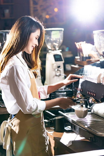 Side view shot of a barista brewing coffee by modern coffeemaker machine to making a cup of coffee with other barista working in background. Using for small business entrepreneur owner concept. - 写真・画像