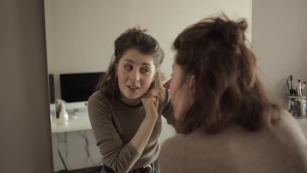 Egy fiatal lány a tükör előtt megvizsgálja a haját és kihúzza az ősz haját. - Felvétel, videó