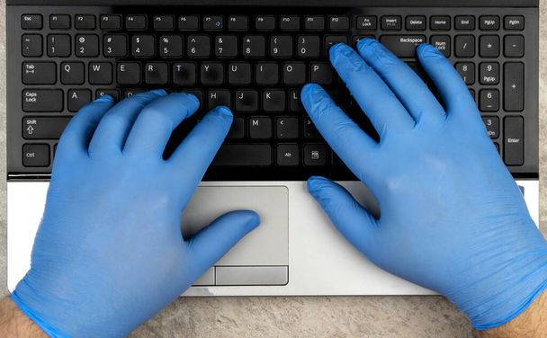 hands in medical gloves on the keyboard. Learning or working online in period of quarantine coronavirus COVID-19. Remote work. preventing the spread of a pandemic, stay at home. - Photo, Image
