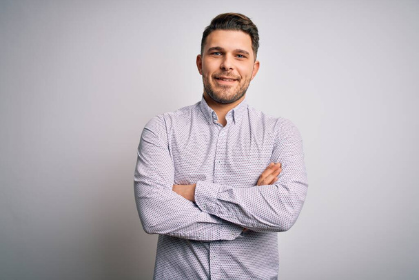 Young business man with blue eyes standing over isolated background happy face smiling with crossed arms looking at the camera. Positive person. - Foto, afbeelding