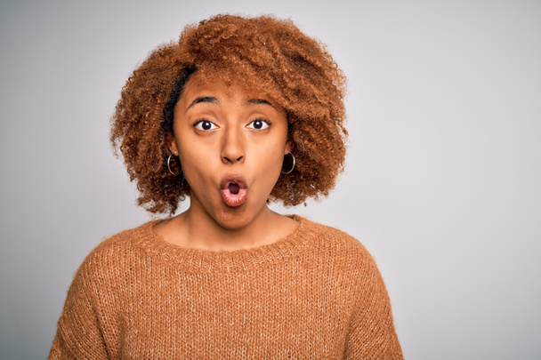 Νεαρή όμορφη Αφρο-Αμερικανίδα με σγουρά μαλλιά που φοράει casual πουλόβερ τρομαγμένη σε κατάσταση σοκ με πρόσωπο έκπληξη, φοβισμένη και ενθουσιασμένη με την έκφραση φόβου - Φωτογραφία, εικόνα