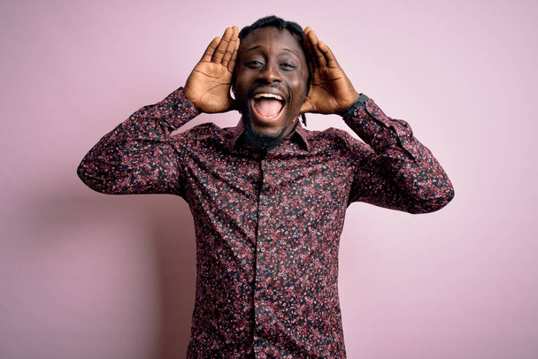 Mladý pohledný africký Američan v ležérní košili stojící nad růžovým pozadím Usmívající se veselá hra nahlédnout boo s rukama ukazujícími tvář. Překvapen a ukončen - Fotografie, Obrázek