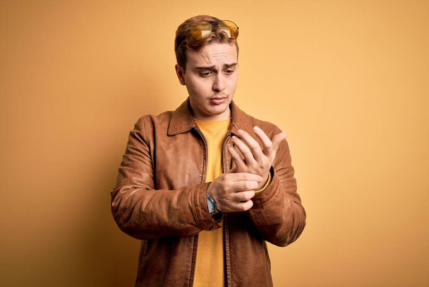 Young handsome redhead man wearing casual leather jacket over isolated yellow background Suffering pain on hands and fingers, arthritis inflammation - Foto, Imagem