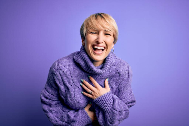 Young blonde woman with short hair wearing winter turtleneck sweater over purple background smiling and laughing hard out loud because funny crazy joke with hands on body. - Fotografie, Obrázek