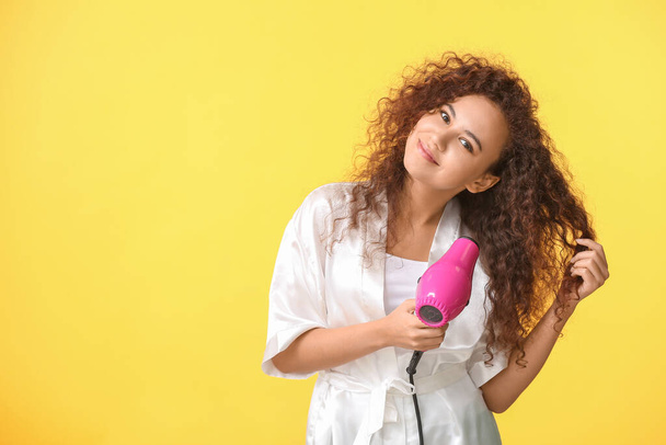 Beautiful young African-American woman with blow dryer on color background - Photo, Image