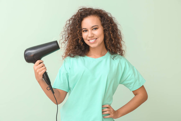 Beautiful young African-American woman with blow dryer on color background - Photo, Image