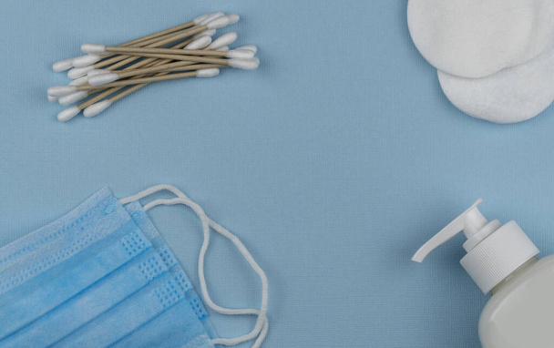Flat lay composition with sanitizer gel and natural cotton sticks on blue background. antiviral medical mask for protection against coronavirus COVID-19.hygiene and sanitation. Top view - Photo, Image
