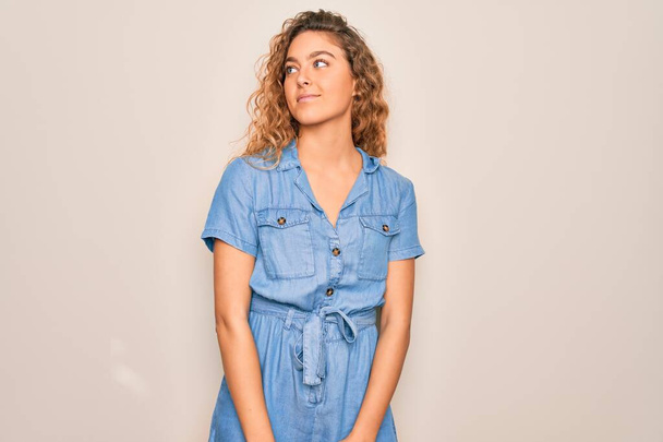 Young beautiful woman with blue eyes wearing casual denim dress over white background smiling looking to the side and staring away thinking. - Foto, Bild