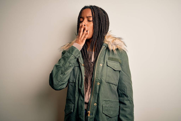 Young african american woman wearing winter parka coat over isolated background bored yawning tired covering mouth with hand. Restless and sleepiness. - Photo, Image