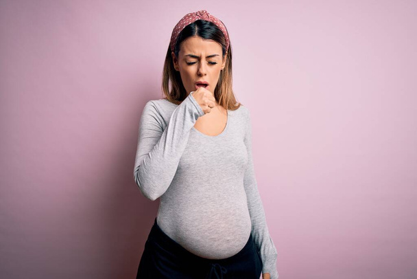 Jonge mooie brunette vrouw zwanger verwacht baby over geïsoleerde roze achtergrond gevoel onwel en hoesten als symptoom voor verkoudheid of bronchitis. Gezondheidszorgconcept. - Foto, afbeelding