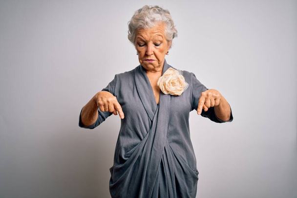 Senior beautiful grey-haired woman wearing casual dress standing over white background Pointing down looking sad and upset, indicating direction with fingers, unhappy and depressed. - Foto, Imagem