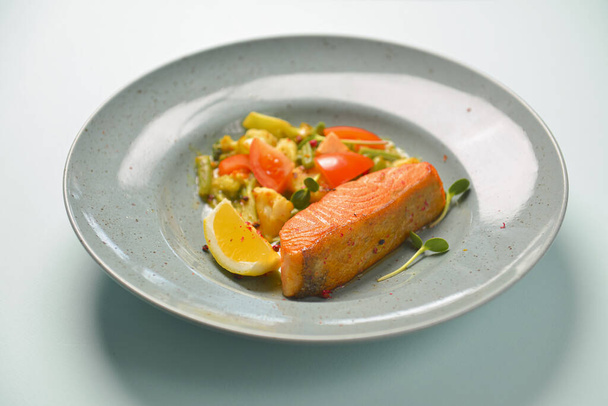 Baked salmon steak with healthy vegetable salad. Organic delicious dinner served on a blue plate over blue background. - 写真・画像