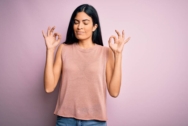 Mladá krásná hispánská módní žena na sobě ležérní svetr přes růžové pozadí relaxovat a usmívat se se zavřenýma očima dělat meditační gesto s prsty. Koncept jógy. - Fotografie, Obrázek