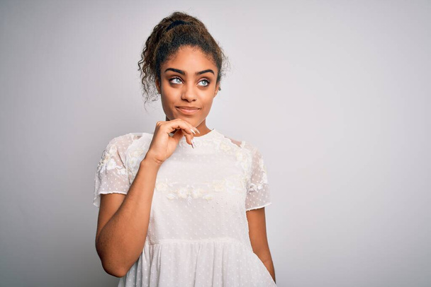 Junge schöne afrikanisch-amerikanische Mädchen in lässigem T-Shirt vor weißem Hintergrund mit der Hand am Kinn über Frage nachdenkend, nachdenklicher Ausdruck. Lächelndes und nachdenkliches Gesicht. Zweifelhaftes Konzept. - Foto, Bild